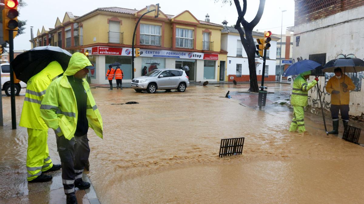 Operarios de los servicios operativos ayudan a retirar el exceso de agua acumulada en la barriada de Campanillas tras el desbordamiento del río a cusa de las fuertes lluvias .