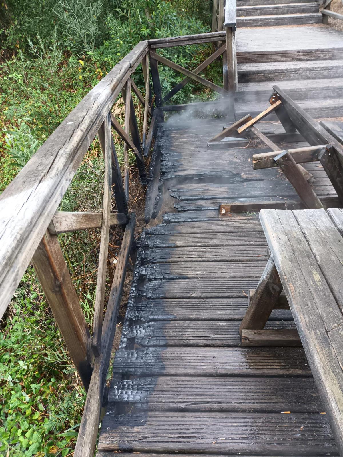 La pasarela de madera incendiada, aún humeante. | // FDV