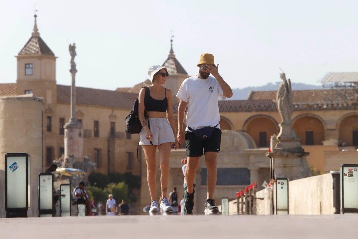 Dos turistas pasean en plena ola de calor por el Puente Romano de Córdoba, este sábado.