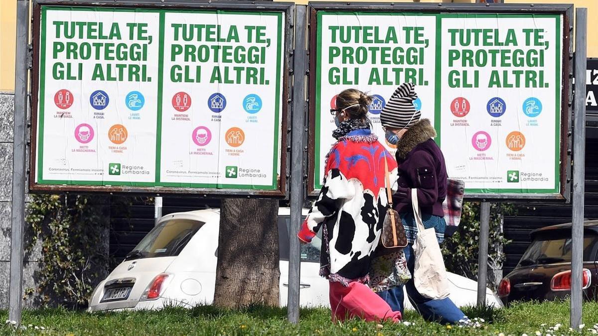 Dos mujeres con mascarillas caminan frente a unos carteles que instan a los ciudadanos a protegerse frente al coronavirus, este miércoles en Milán.
