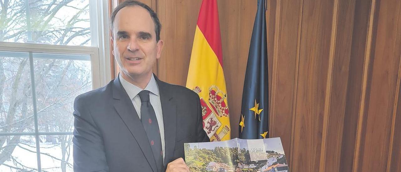 El embajador español muestra el folleto con la portada de Cudillero.