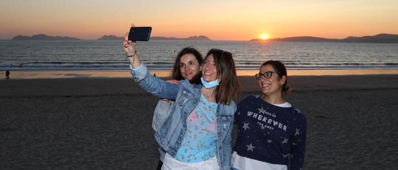 Tres mujeres se hacen un selfie en Samil, con la puesta de sol de fondo.