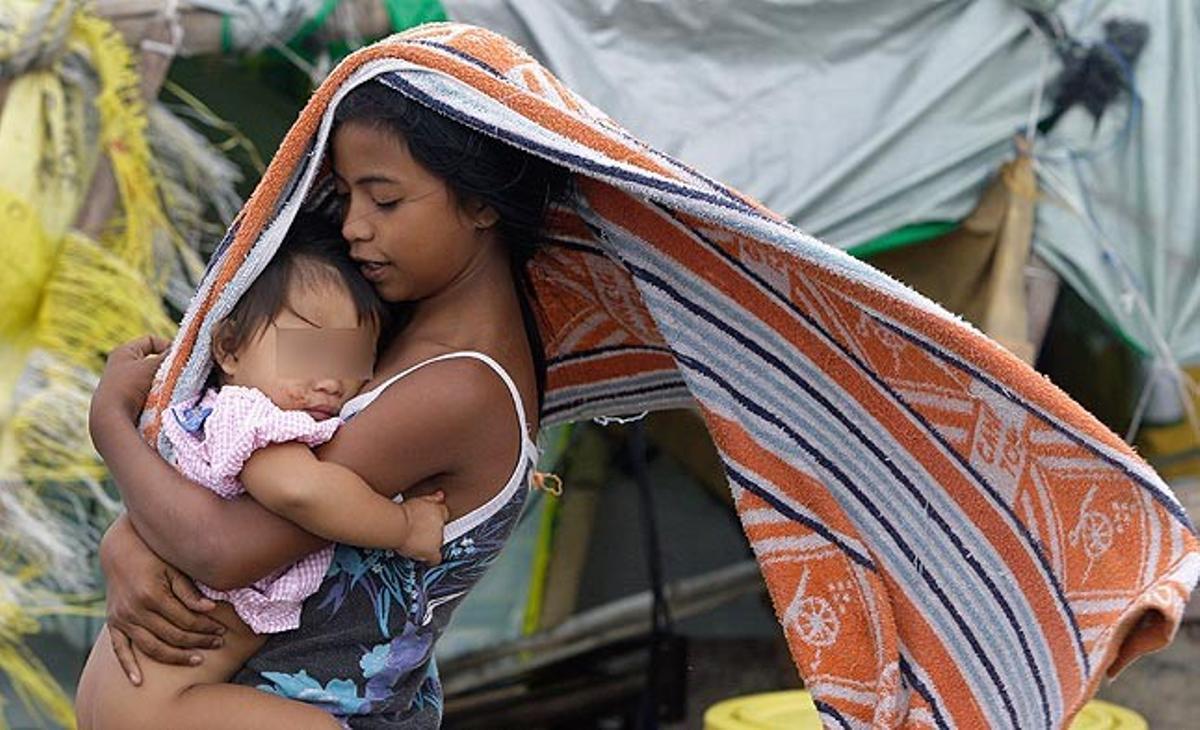 Una adolescent filipina porta aquest dilluns un nadó protegint-lo del fort vent que sacseja la regió de Navotas, al nord de Manila.