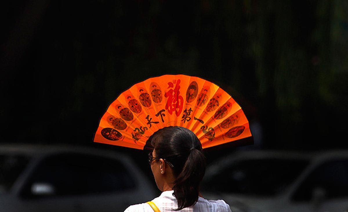 Una dona es tapa la cara amb un ventall per alleujar la calor en un carrer de Pequín.