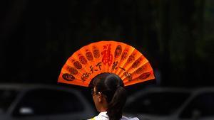Una dona es tapa la cara amb un ventall per alleujar la calor en un carrer de Pequín.