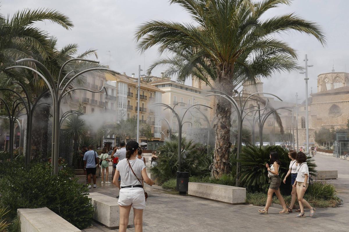 Los turistas se refrescan en alerta de calor con el agua de la plaza de la Reina de València.
