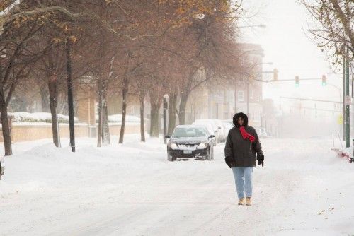 A woman walks down the middle of the street through the blowing snow in Buffalo