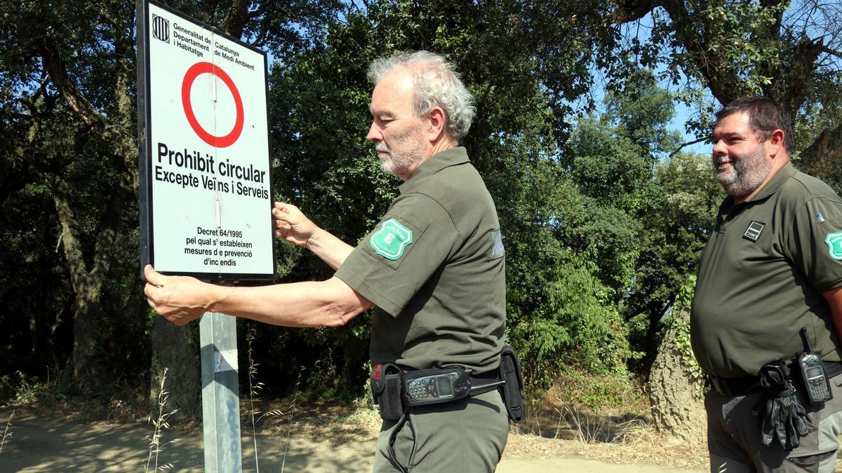 Agents Rurals desplegant un dels cartells que impedeix el pas per dins del massís de les Gavarres arran de l&#039;entrada en nivell 3 del Pla Alfa