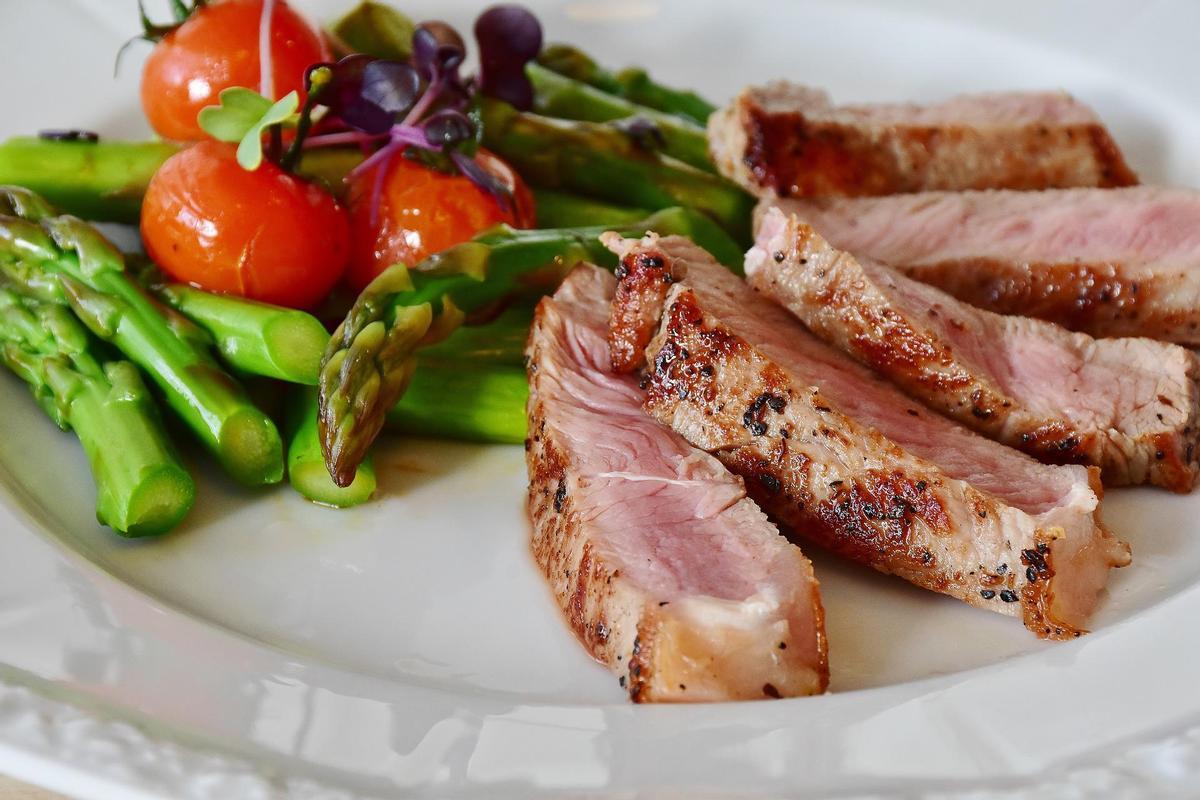 Un plato de carne y espárragos con tomate. 