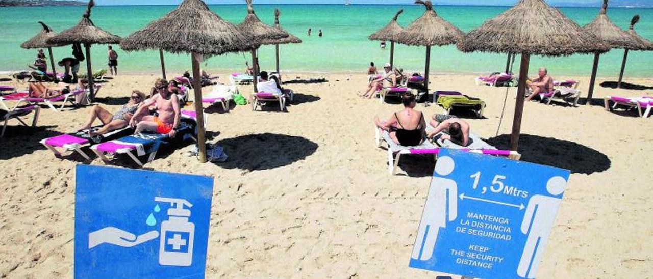 Unos turistas toman el sol en una playa de Palma de 
Mallorca, con los carteles en los que se recuerdan las medidas de seguridad en primer plano. | Jaime Reina / AFP