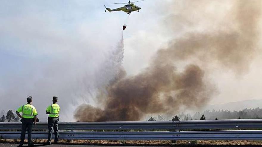 Un helicóptero, ayer, trabaja en la extinción de un fuego próximo a la autovía entre Santiago y A Estrada. / bernabé