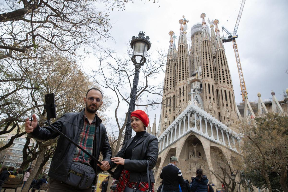 Turistas se toman un selfie junto a un cartel en la Basílica de la Sagrada Familia de Barcelona