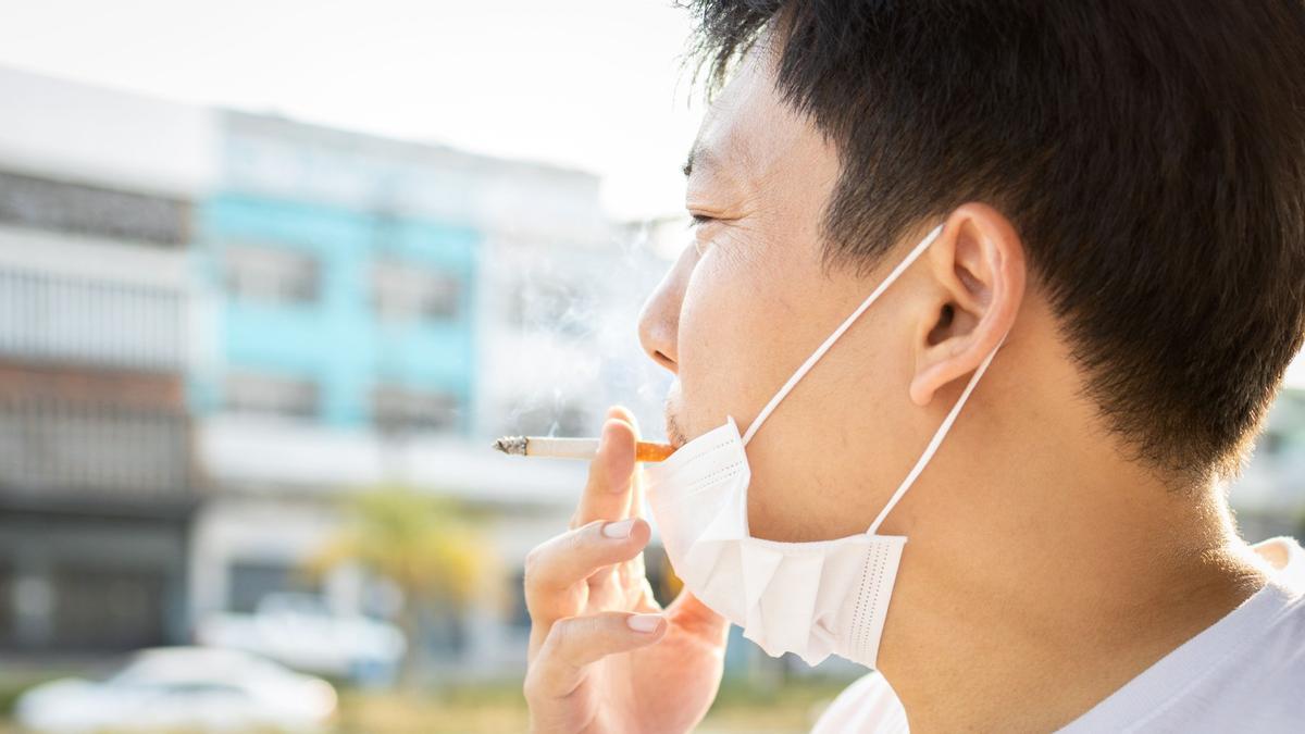 Un hombre con la mascarilla bajada para fumarse un cigarrillo.