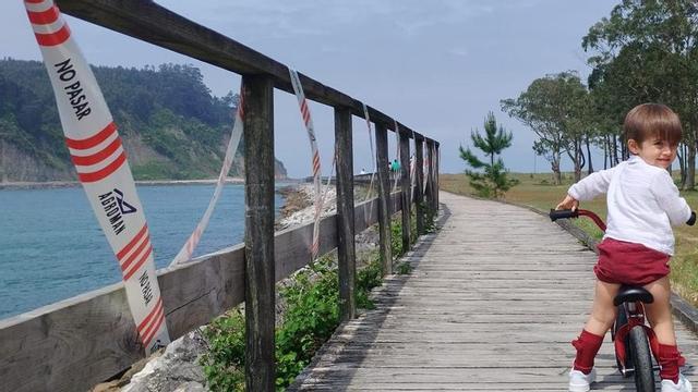 Un niño, en bicicleta, por una zona dañada del parque playa de Rodiles. | PABLO  ANTUÑA