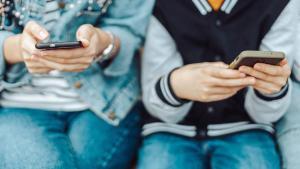 Dos adolescentes miran sus teléfonos móviles.