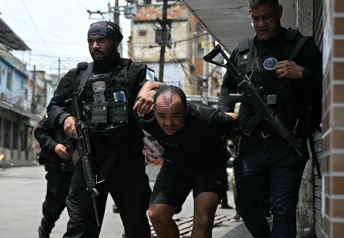 TOPSHOT - A suspect is escorted by police officers after being arrested during the Operacao Contencao (Operation Containment) at the Vila Cruzeiro favela, in the Penha complex, in Rio de Janeiro, Brazil, on October 28, 2025. At least 2,500 agents took part in an operation to arrest drug traffickers from the Comando Vermelho (CV), which resulted in, at least, 18 suspects and several police officers dead. (Photo by Mauro PIMENTEL / AFP)