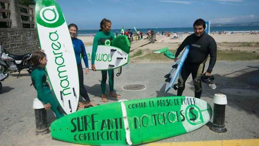 Los impulsores de la iniciativa, ante una tabla con críticas al cobro de tasas por el surf en las playas y, a la derecha, cartel contra el cobro de la ORA.