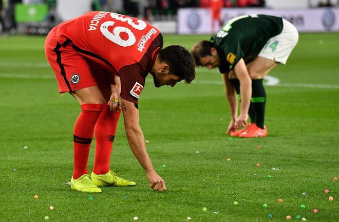 El jugador de Frankfurt Goncalo Pacienca (L) recoge canicas de plástico de colores lanzadas en el campo por los seguidores de Frankfurt durante el partido de fútbol de la Bundesliga VfL Wolfsburg - Eintracht Frankfurt en Wolfsburg, Alemania.
