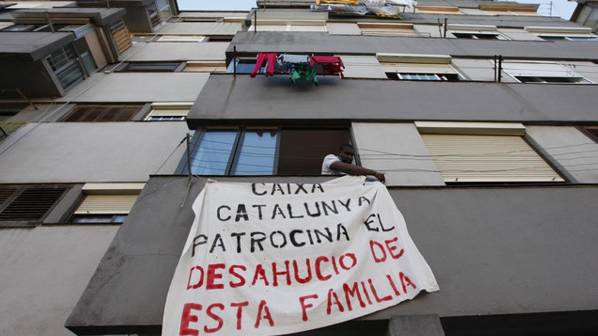 Efosa sujeta una pancarta contra el desahucio, colocada en la ventana de su casa, en Ciutat Meridiana.