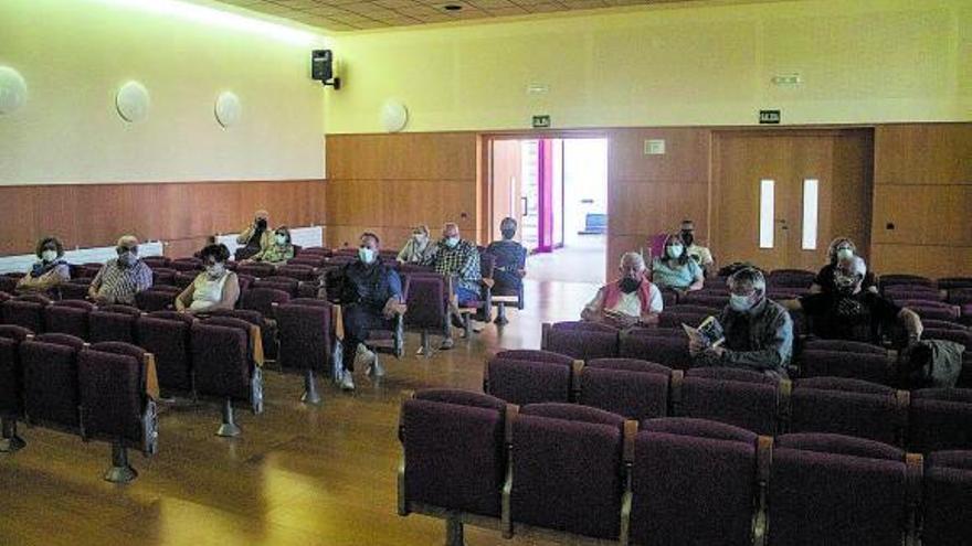 Lectoras y lectores durante uno de los encuentros en su lugar habitual de reunión, en el salón de actos de Muelas. Debajo uno de los miembros en plena faena frente a un libro. | |  SARA RODRÍGUEZ