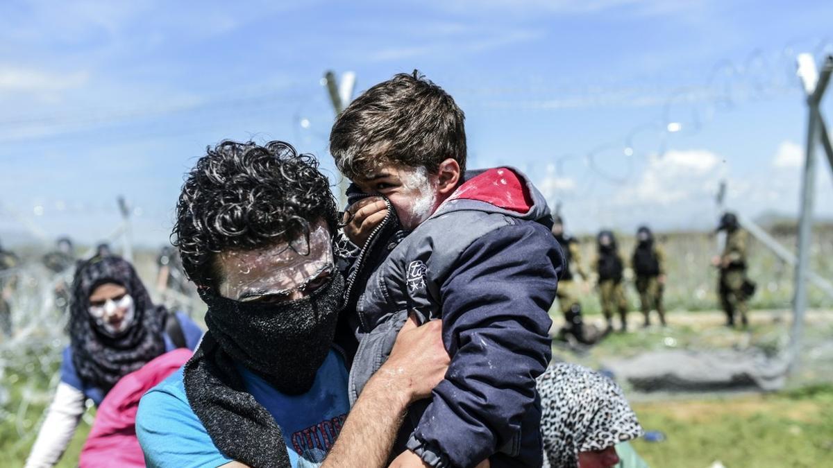 Un padre coge en brazos a su hijo, durante los ataques con gases lacrimógenos en la frontera de Macedonia, este domingo.