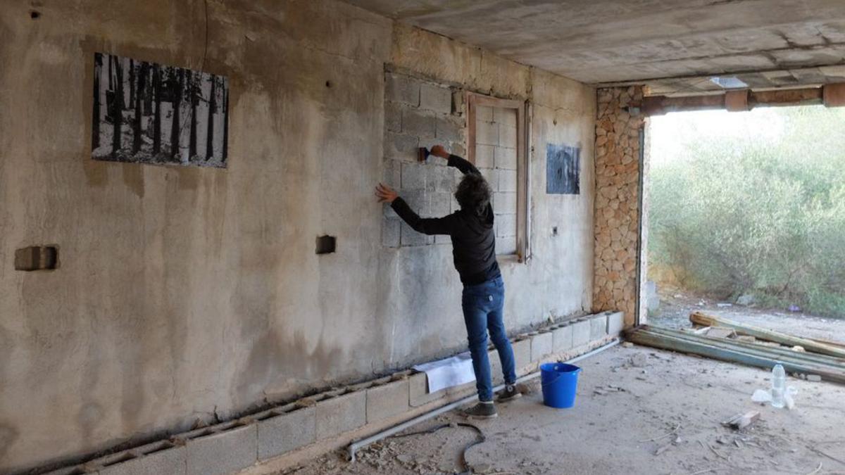 El artista encola la pared para pegar una foto durante la intervención en una ruina, donde montó una inquietante exposición.