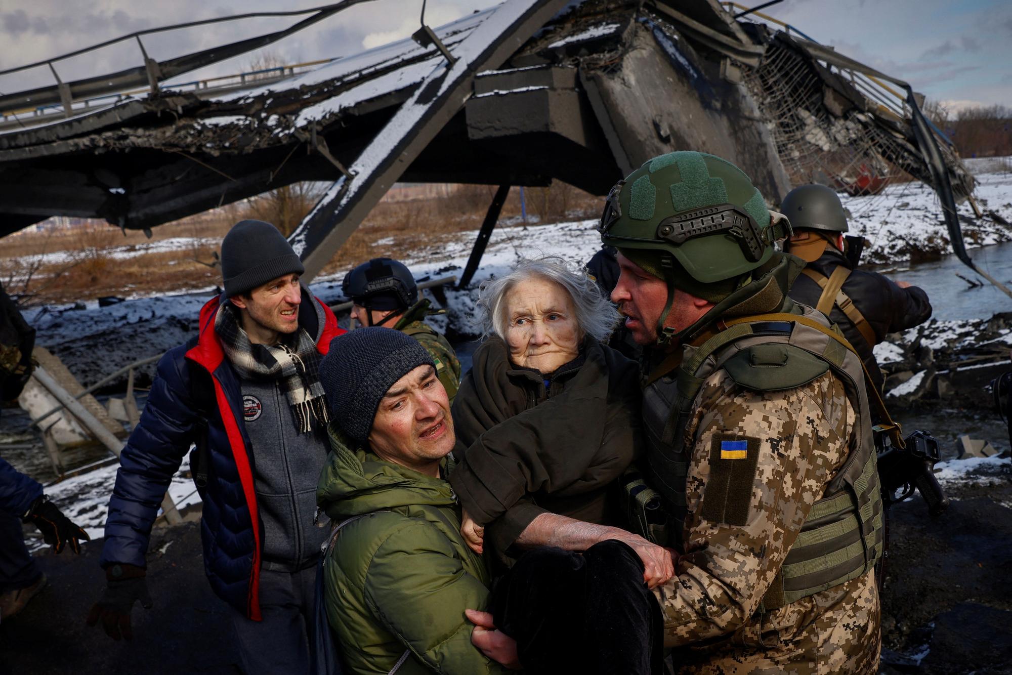 Two men carry a woman as people flee from advancing Russian troops whose attack on Ukraine continues in the town of Irpin outside Kyiv