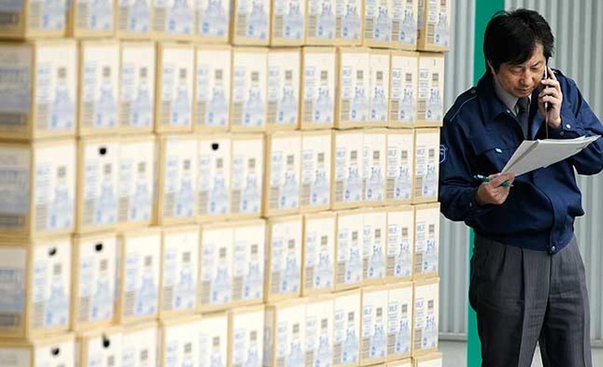 Un treballador parla pel mòbil davant d’un carregament de 240.000 ampolles d’aigua per ser distribuïdes a Tòquio (Japó), com a part del programa d’emergència per proveir els nens amb aigua sense contaminació.