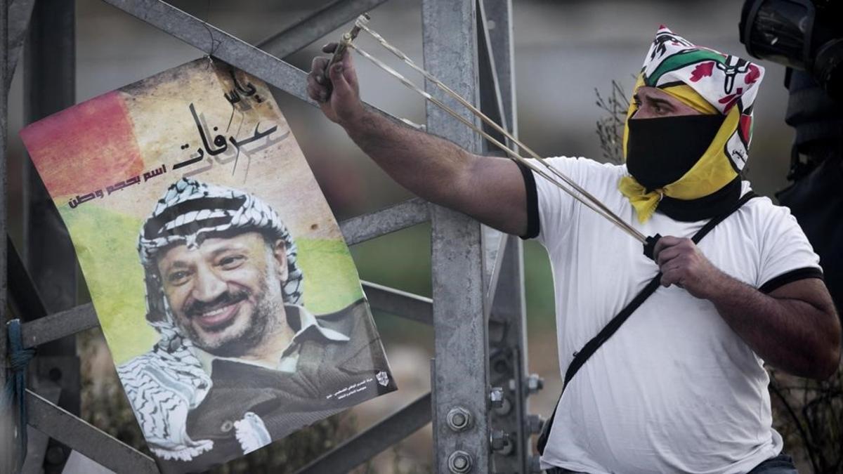 Un palestino tensa una honda junto a un póster con la imagen de Arafat, en una protesta durante el 11º aniversario de su muerte, el 11 de noviembre del 2015.