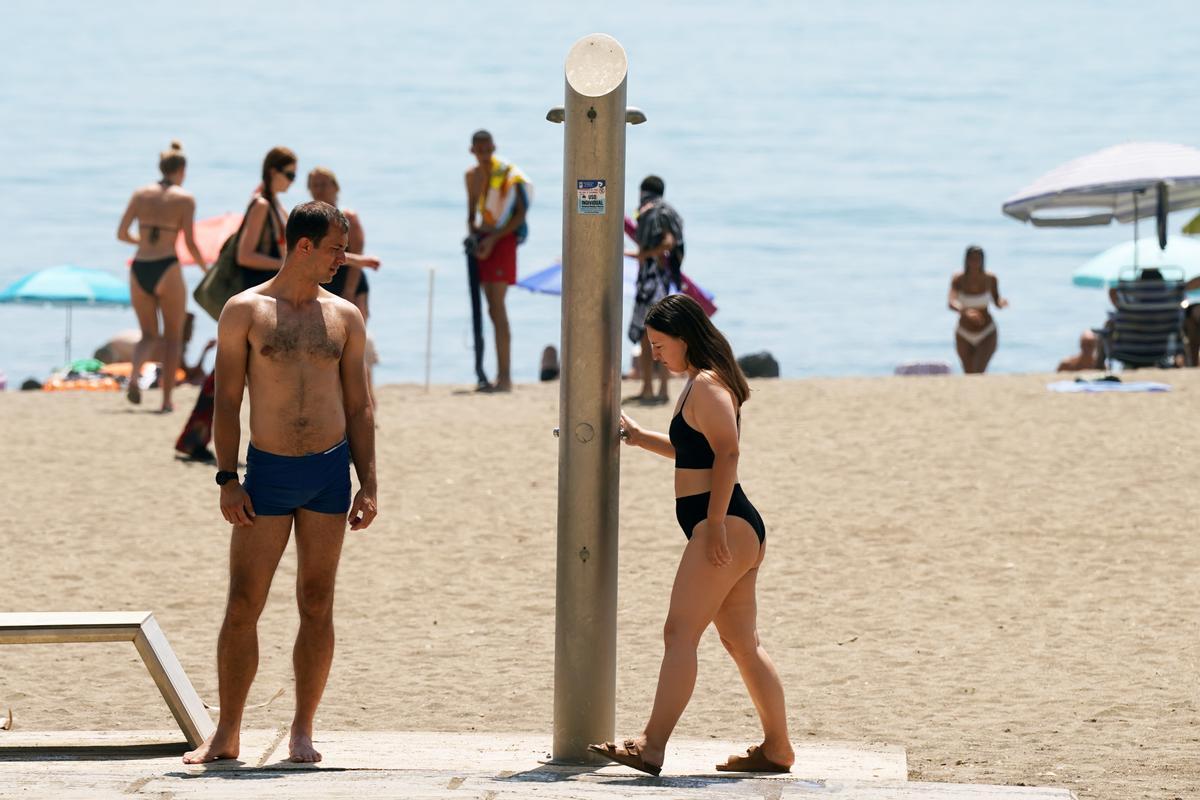 Dos personas comprueban el corte de agua en las duchas de la playa en La Malagueta