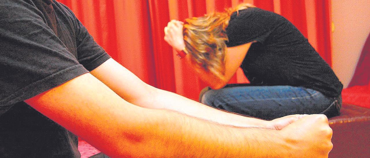 Un hombre, sentado con gesto amenazante, frente a una mujer atemorizada en una imagen de recurso