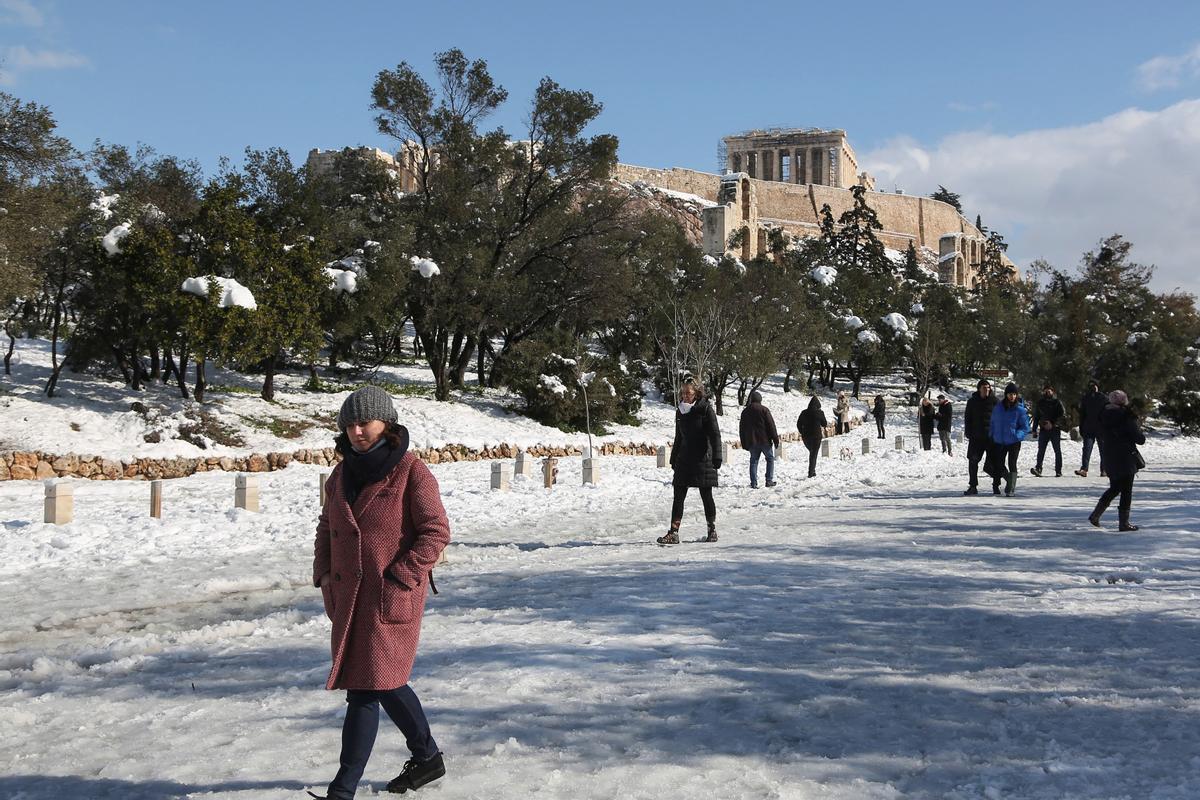 Ciudadanos en la calle peatonal Areopagitou, cubierta por la nieve, con el Partenón en la colina de la Acrópolis al fondo.
