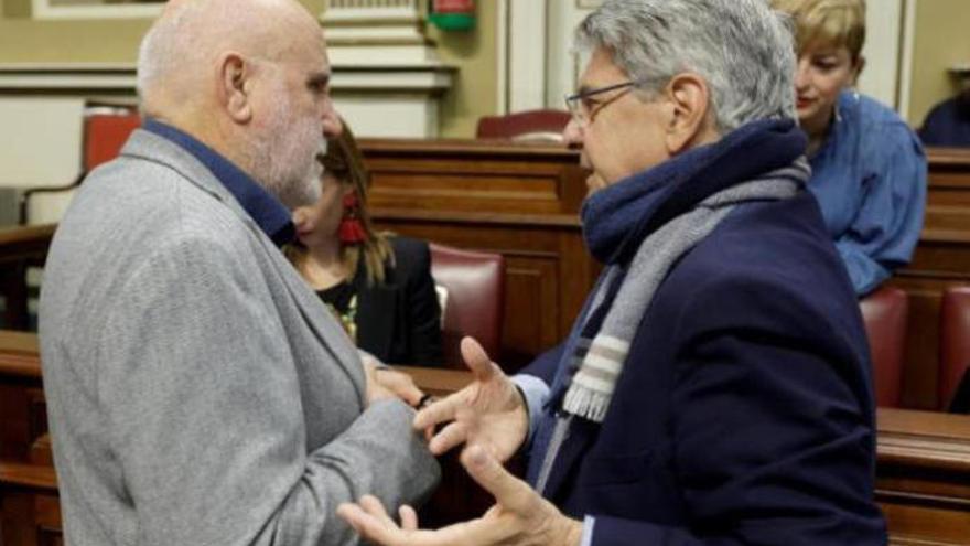 El consejero de Administraciones Públicas, Julio Pérez (d), con el diputado de Podemos, Manuel Marrero (i), antes del inicio del Pleno del Parlamento de Canarias.