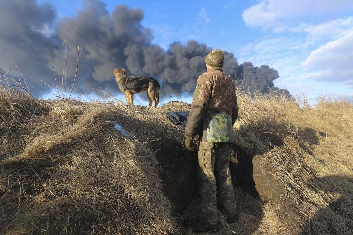 Un militar ucraniano y su perro observan una columna de humo negro procedente de un depósito de petróleo atacado por un misil ruso, en las proximidades de Kiev, el 27 de febrero de 2022.