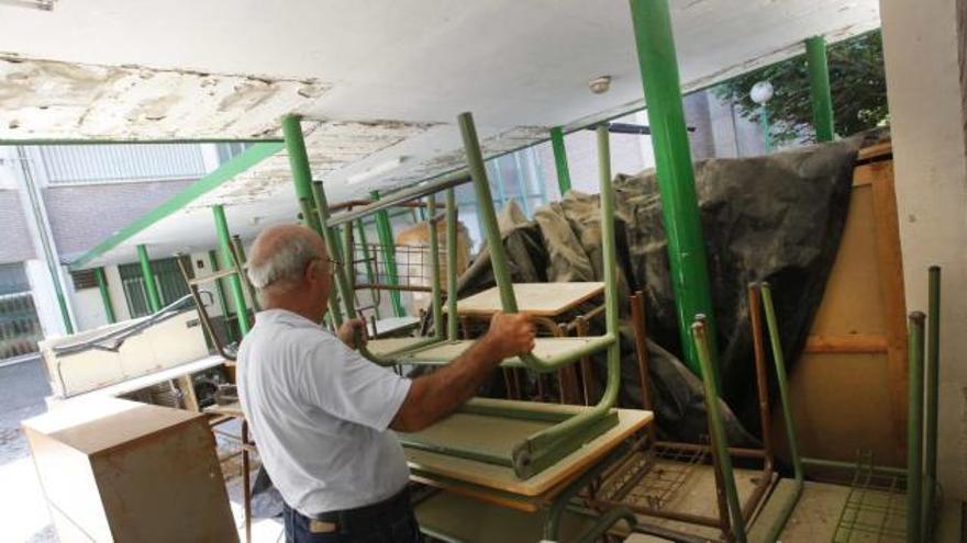 Un profesor sujeta uno de los muebles almacenados durante las obras bajo un techo desconchado que van a reparar.