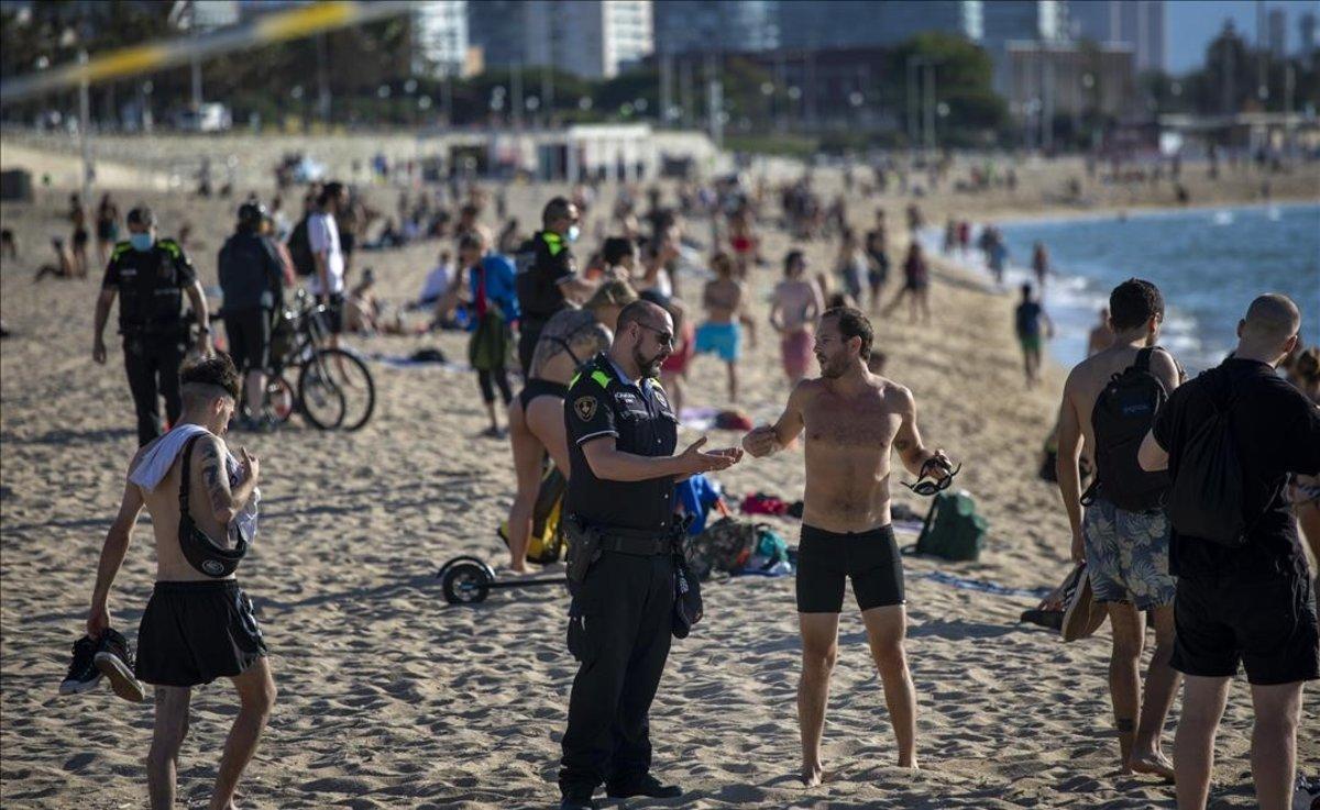 Agentes de policía explican a los ciudadanos que no deben sentarse o tomar el sol en la playa, en Barcelona.