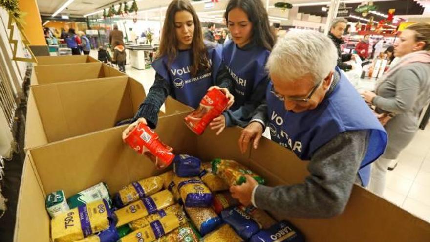 Dues voluntàries i un voluntari, posant a lloc paquets de pasta en un supermercat.
