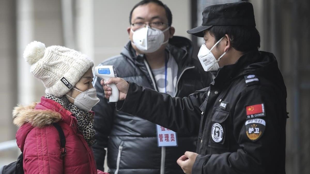 Personal de seguridad comprueba la temperatura coproral de los pasajeros en el muelle del río Yangtze, en la ciudad china de Wuhan.