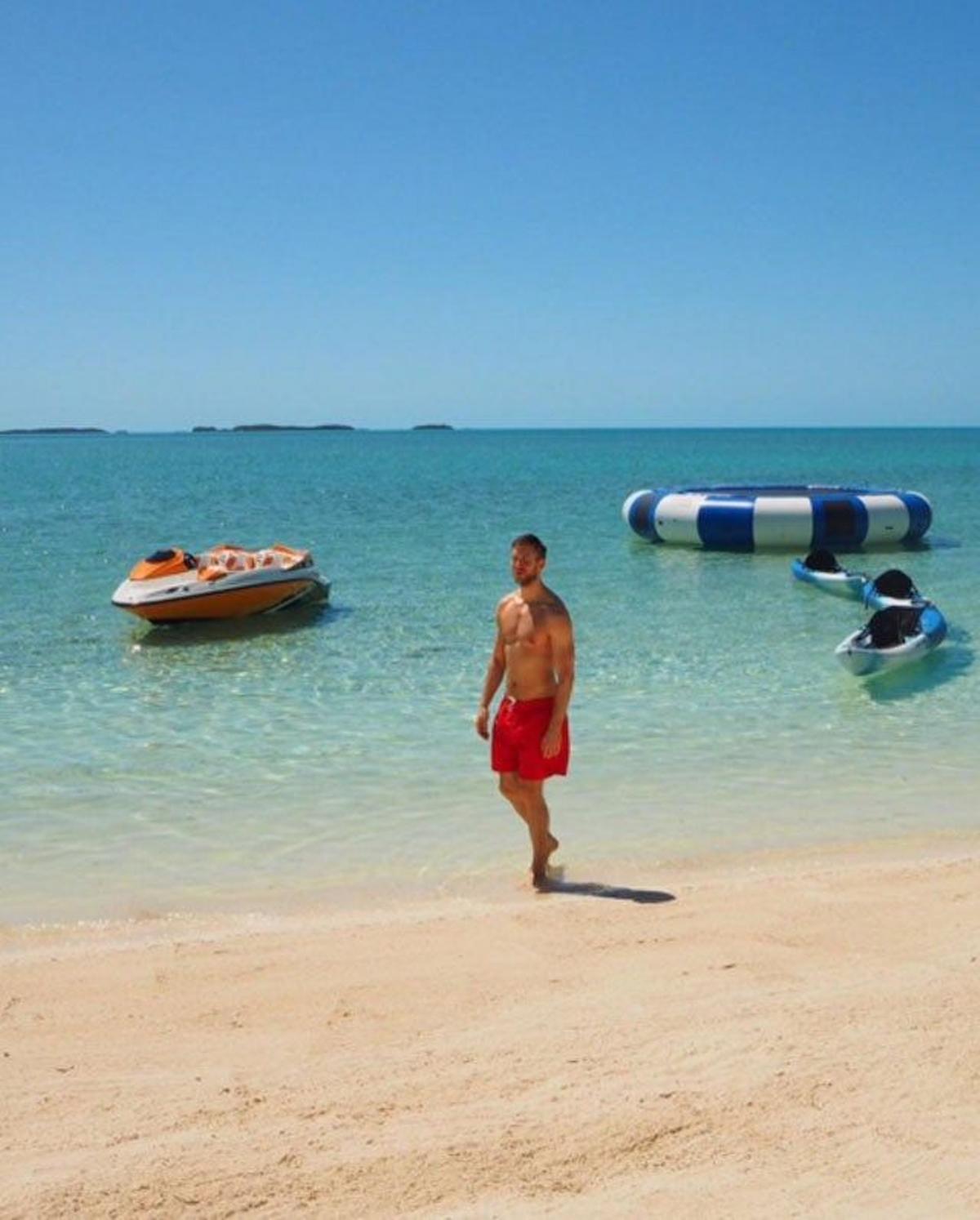 Calvin Harris, con un bañador rojo, dando un paseo por la orilla.
