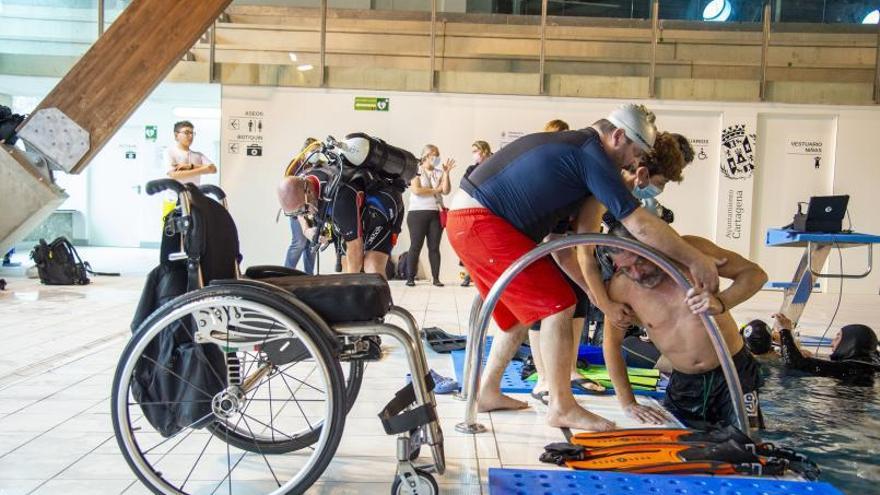 Marcos, en silla de ruedas, sale del agua ayudado por un acompañante tras disfrutar de la inmersión.