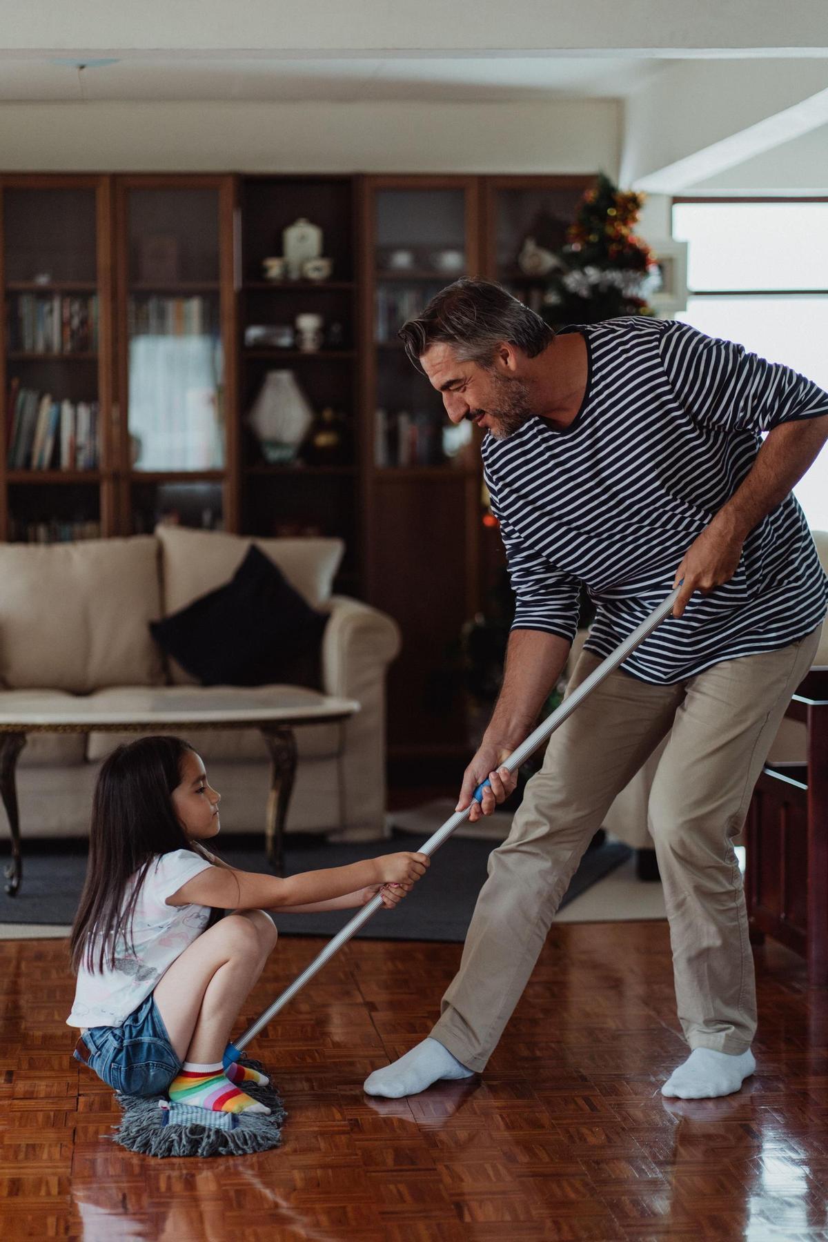 Un padre juega con su hija mientras friega la casa