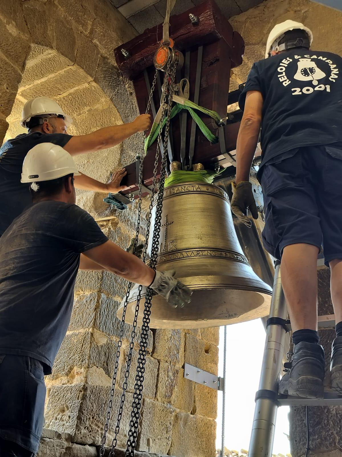 Unos operarios colocan la campana en su lugar en la iglesia.