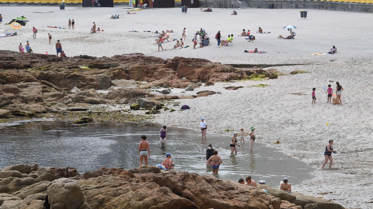 Bañistas en la playa coruñesa de Riazor un día con cielo nublado.