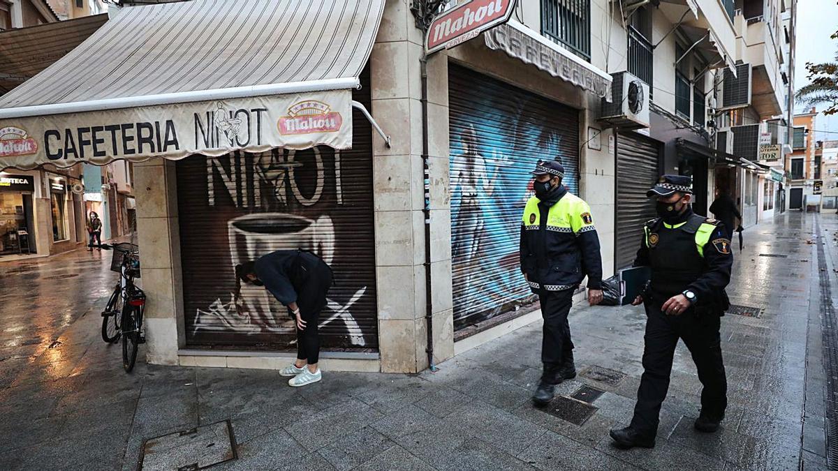 Dos policías locales de Elche pasan junto a una cafetería que cerró a las cinco en punto. | ANTONIO AMORÓS