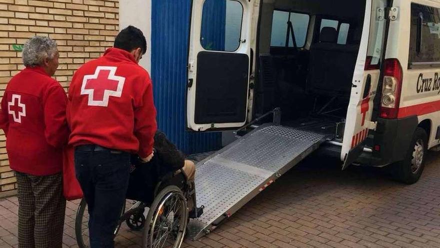 Un técnico de Cruz Roja sube a una persona con movilidad reducida al vehículo adaptado para su traslado.