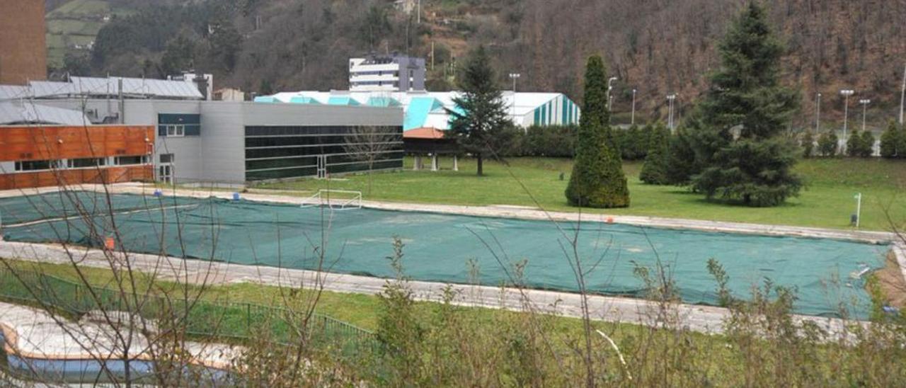 Arriba, la piscina exterior de Vega de Arriba, tapada tras su cierre. En el círculo, una infografía del proyecto presentado por el PP de Mieres.