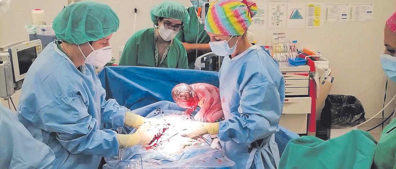 Varias sanitarias atienden tanto a la madre como al recién nacido, durante un parto en el hospital de Gandia, con el padre al fondo.