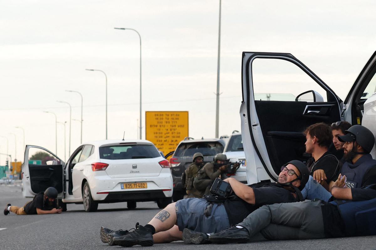 Unos periodistas se refugian detrás de los automóviles mientras los soldados israelíes toman posiciones durante los enfrentamientos con combatientes palestinos cerca del kibutz Gevim, cerca de la frontera con Gaza, el 7 de octubre de 2023.