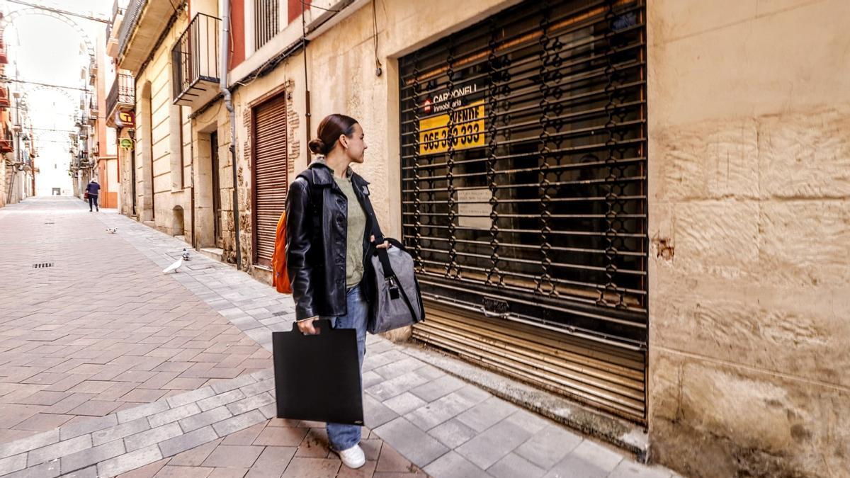 Una joven pasea con sus pertenencias mirando un cartel de &quot;Se alquila&quot;.