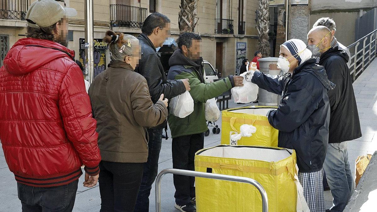 Voluntarios del Comedor Reina de la Paz de las Misioneras de la Caridad reparten alimentos entre personas necesitadas, en el barrio del Raval de Barcelona, el 12 de abril